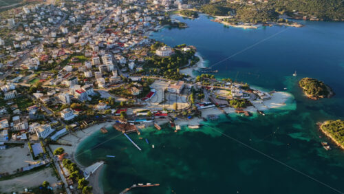 Video - Aerial drone view of Ksamil town, it's dense cluster of hotels and houses, and the iconic bright blue bays with floating platforms and beach clubs
