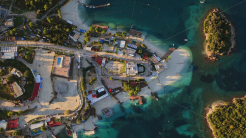 Video - Aerial drone view of Ksamil town, it's dense cluster of hotels and houses, and the iconic bright blue bays with floating platforms and beach clubs