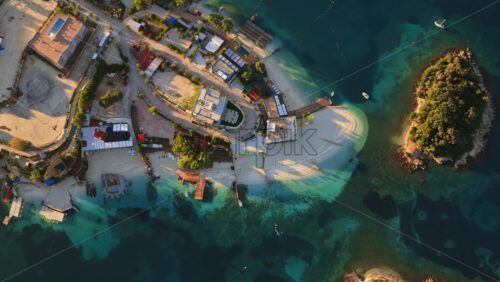 Video - Aerial drone view of Ksamil town, it's dense cluster of hotels and houses, and the iconic bright blue bays with floating platforms and beach clubs