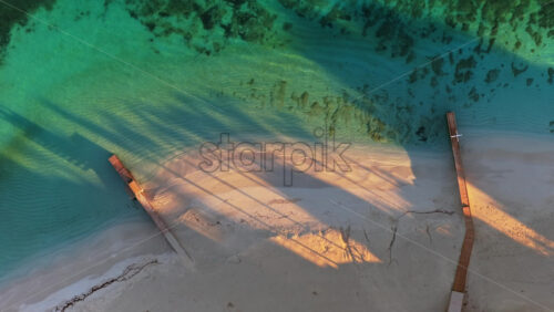 Video - Aerial drone view of Ksamil Beach, highlighting white sand and shallow turquoise water, with long shadows from nearby structures stretching across the shore