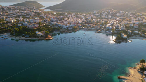 Video - Aerial drone view of Ksamil town, it's dense cluster of hotels and houses, and the iconic bright blue bays with floating platforms and beach clubs