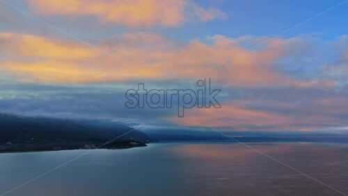 Video - Aerial drone view of Lake Ohrid, with low clouds hugging the mountains and soft pastel light reflecting across the water. North Macedonia