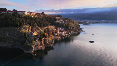 Video - Aerial drone view of the Kaneo church on its rocky cliff, with the charming old houses of Ohrid cascading down toward the lake's edge. North Macedonia