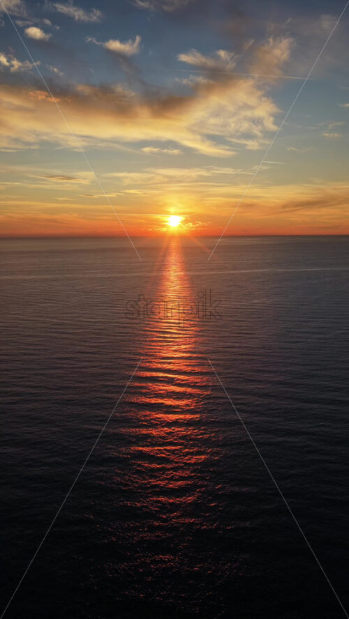 Video - Aerial drone view of a sunset across the open Adriatic Sea, with the sun descending and reflecting golden light on the waves. Vertical