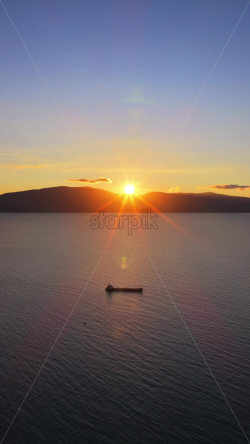 Video - Aerial drone view of a fisherman rowing a weathered wooden boat across the serene waters of Vlora Bay at dusk, creating gentle ripples that reflect the pastel evening light. Vertical