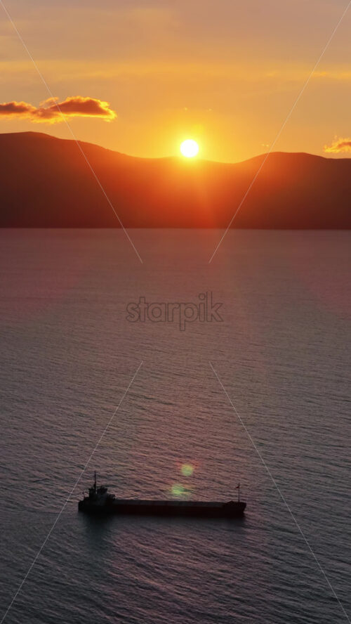 Video - Aerial drone view of a fisherman rowing a weathered wooden boat across the serene waters of Vlora Bay at dusk, creating gentle ripples that reflect the pastel evening light. Vertical