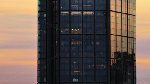 Video - Aerial drone view of the modern glass facade of a skyscraper in Warsaw in the Wola district, capturing reflections of the city during sunset