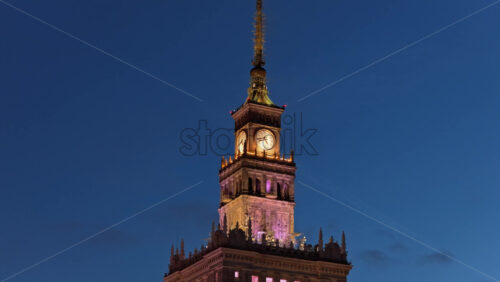 Video - Aerial drone view of the Palace of Culture of Warsaw and Science, glowing with colorful lights among the surrounding skyscrapers in the evening