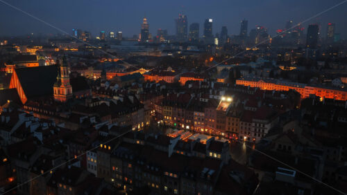 Video - Aerial drone view of the Old Town Market Square in Warsaw during dusk, showcasing market stalls, warm lights, and the surrounding colorful townhouses