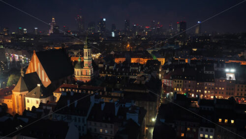Video - Aerial drone view of Warsaw's Old Town at night, showing warm lights on rooftops, narrow streets, and historic buildings creating a cozy evening atmosphere