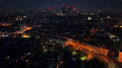 Video - Aerial drone view of Warsaw's Old Town toward the Srodmiescie district, with bright city lights and residential buildings visible below