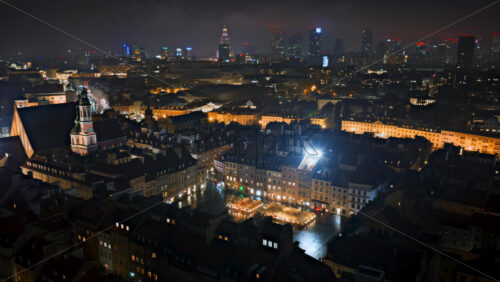 Video - Aerial drone view time lapse of the Old Town Market Square during dusk, showcasing market stalls, warm lights, and the surrounding colorful townhouses