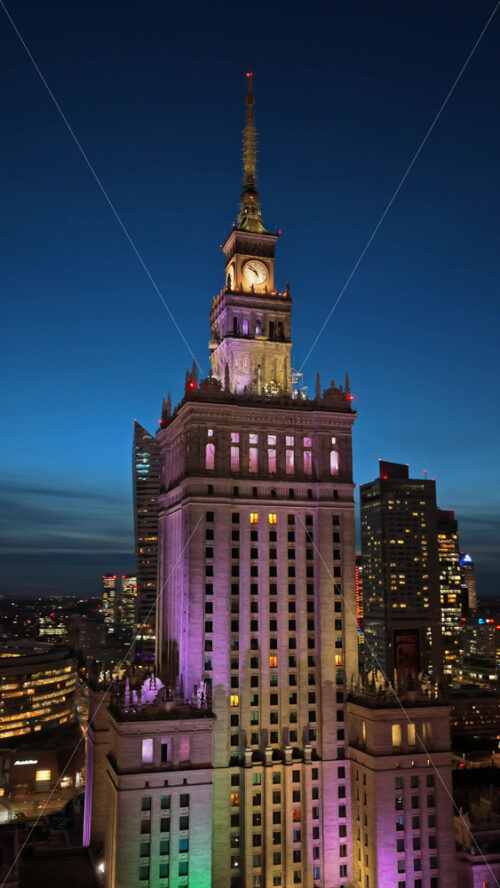 Video - Warsaw, Poland - October 31, 2025: Aerial drone view of the Palace of Culture of Warsaw and Science, glowing with colorful lights among the surrounding skyscrapers in the evening. Vertical
