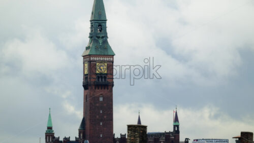 Video - Copenhagen, Denmark - August 3, 2025: Copenhagen city hall clock tower rising above urban rooftops against a cloudy sky