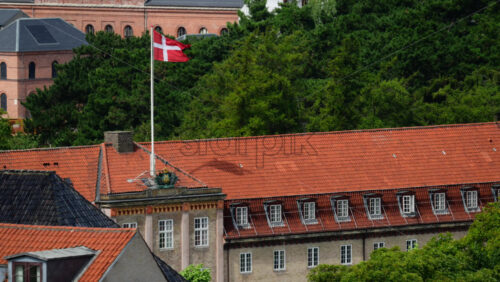 Video - Danish flag waving on a flagpole above a building with a red tiled roof and a green tree background