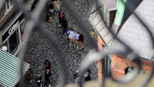 Video - Copenhagen, Denmark - August 4, 2025: Pedestrians walking on a cobblestone street in a shopping district, viewed from a high angle