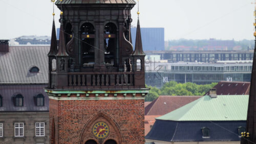 Video - Copenhagen, Denmark - August 4, 2025: Ornate copper spire and bell tower of a brick church overlooking a cityscape