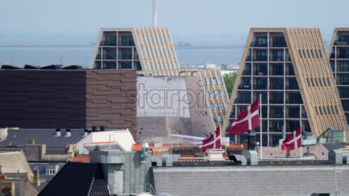 Video - Danish flags waving over residential buildings with modern pyramid shaped structures in Paper Island. Copenhagen, Denmark