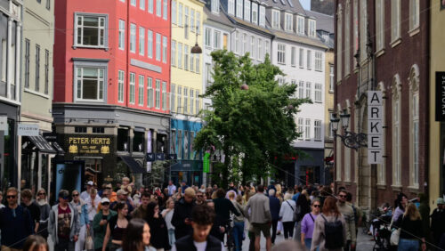 Video - Copenhagen, Denmark - August 4, 2025: Row of traditional old street buildings with stores at street level. Pedestrians walking by and shopping