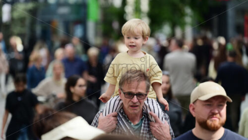 Video - Copenhagen, Denmark - August 4, 2025: Father carrying child on shoulders, navigating through a busy city street among many people