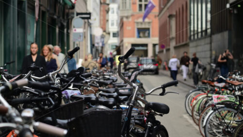 Video - Copenhagen, Denmark - August 4, 2025: Urban street scene showing many bicycles parked with pedestrians walking by