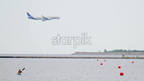 Video - Copenhagen, Denmark - August 4, 2025: Airplane flying above ocean with kayakers paddling near a pier and lighthouse