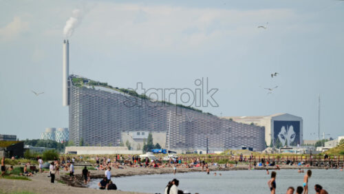 Video - Copenhagen, Denmark - August 4, 2025: People enjoying a beach with the Copenhill waste to energy plant in the background