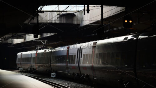 Video - Copenhagen, Denmark - August 5, 2025: Modern electric train traveling through a shadowed transit hub