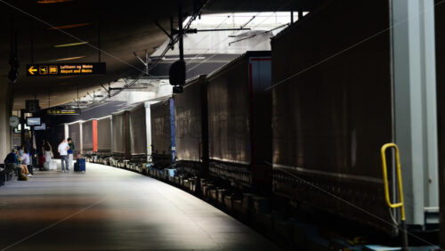 Video - Copenhagen, Denmark - August 5, 2025: Passengers waiting as a freight train, loaded with shipping containers, pulls into a dark station