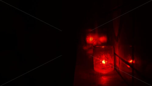 Video - Red candle in a glass jar casting a warm glow, reflected in a nearby surface. Dark club atmosphere