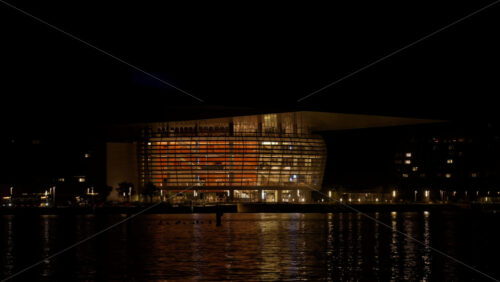 Video - Copenhagen, Denmark - August 5, 2025: Opera House illuminated at night, reflecting its light on the water
