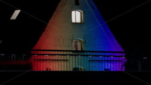 Video - Building facade reflecting a rainbow spectrum across its windows and architectural details at night