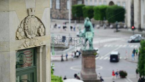 Video - Copenhagen, Denmark - August 3, 2025: Stone ornament featuring a crown on a building facade overlooking a busy city street. Apalon statue on background