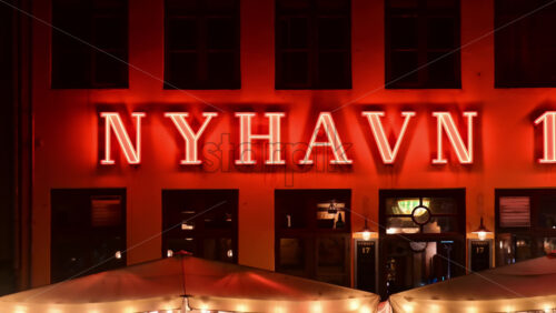Video - Copenhagen, Denmark - August 5, 2025: Nyhavn neon sign glowing red on a building wall at night
