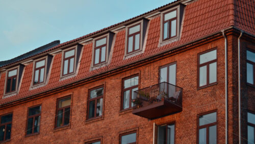 Video - Old brick apartment building facade showcasing windows, balconies, and a tiled roof in an urban setting. Copenhagen, Denmark