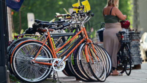 Video - Copenhagen, Denmark - August 6, 2025: Row of city bicycles parked for sale on a street while a woman prepares to ride a bike