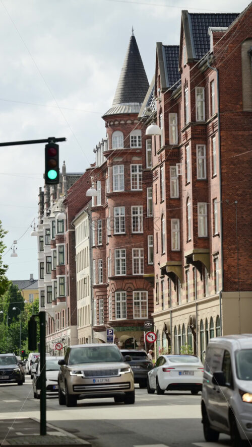 Video - Copenhagen, Denmark - August 7, 2025: City street with brick residential buildings, a traffic light, and cars driving on the road