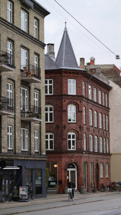 Video - Copenhagen, Denmark - August 7, 2025: Urban street view with historic brick apartment buildings and a person cycling