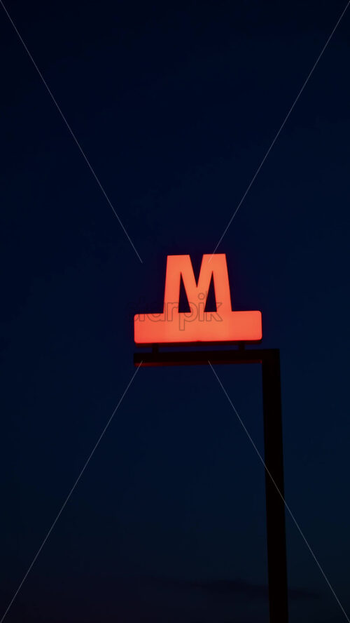 Video - Bright Metro sign illuminating dark city sky, indicating underground metro transportation. Copenhagen, Denmark