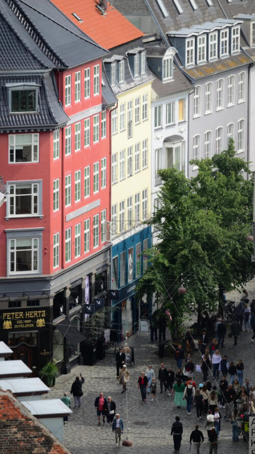 Video - Copenhagen, Denmark - August 7, 2025: People walking on a bustling Stroget street with traditional colorful buildings and lush green trees