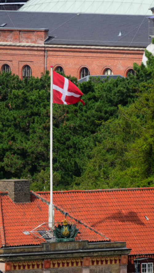 Video - Denmark national flag, Dannebrog, waving on a flagpole above a red tiled roof. Copenhagen