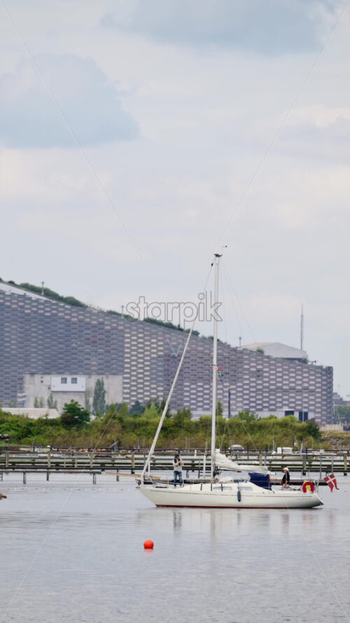 Video - Copenhagen, Denmark - August 7, 2025: Sailboat navigating the urban harbor with Copenhill in the background