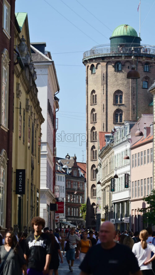 Video - Copenhagen, Denmark - August 7, 2025: People walking along a busy shopping street with the historic Round Tower in the background