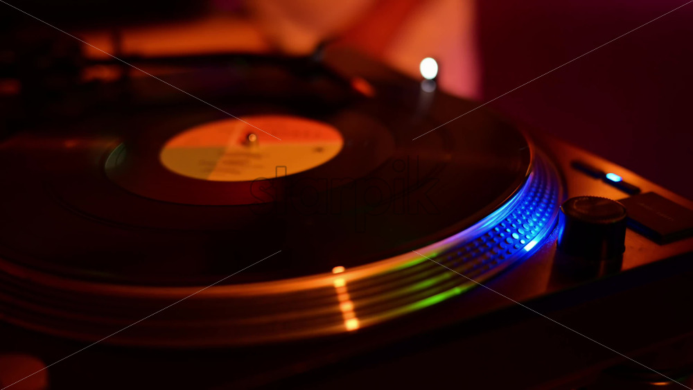 Video - Turntable spinning a vinyl record, showcasing a vibrant club atmosphere with blue and orange lights