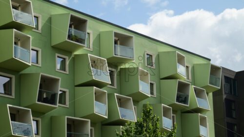 Video - Green building facade with distinctive modern geometric balconies and windows under a blue sky