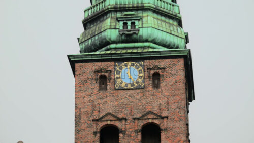 Video - Brick tower with a green copper spire and a blue clock face against a cloudy sky. Copenhagen, Denmark