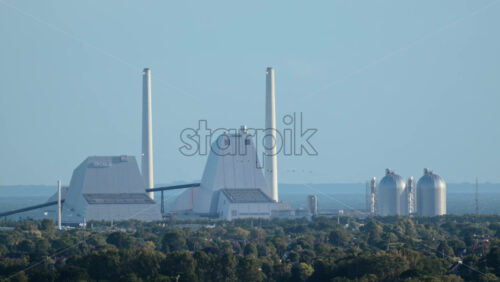 Video - Copenhagen, Denmark - August 4, 2025: Industrial Orsted power plant facility with towering smokestacks and storage tanks against a clear sky