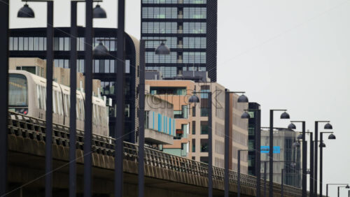 Video - Copenhagen, Denmark - August 4, 2025: Metro train moving on an elevated track through abstract urban cityscape with modern buildings