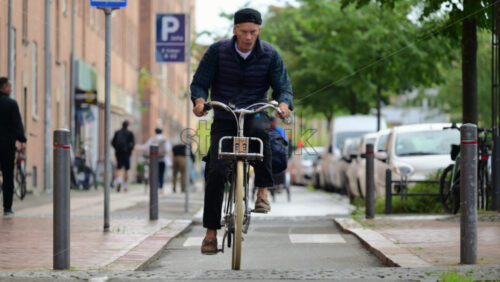 Video - Copenhagen, Denmark - August 4, 2025: Man cycling on a bike lane with pedestrians and parked vehicles along the city street