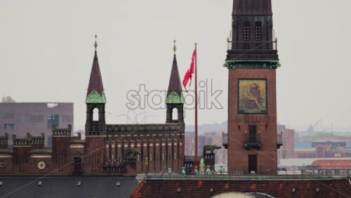 Video - Copenhagen, Denmark - August 4, 2025: City Hall tower and rooftop with a Danish flag flying and wind turbines in the background